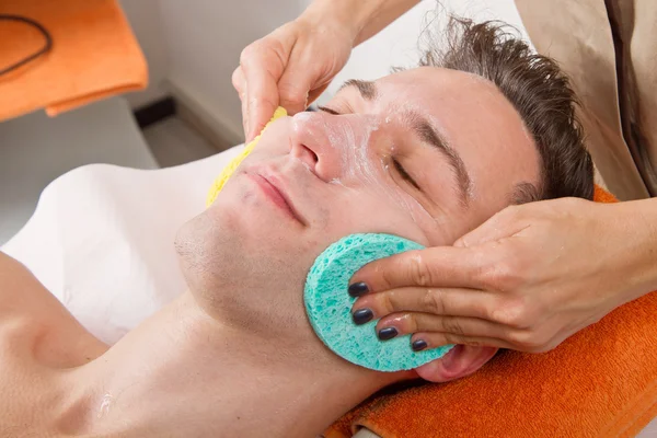 Female hands cleaning man's face in a spa center