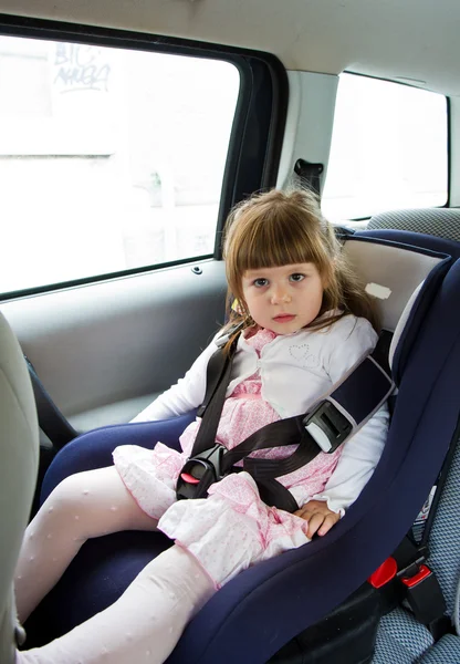 Little cute girl sitting in the car in child safety seat and smi