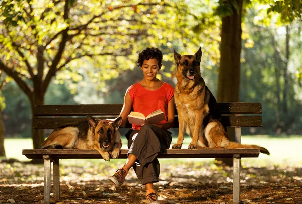 Woman is sitting on a bench with two german shepherds