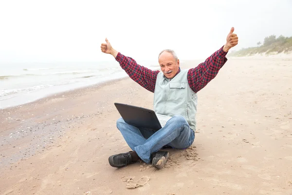 Happy old man on the beach with a laptop