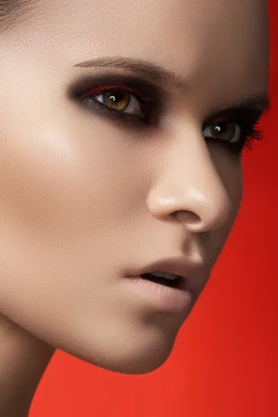 Close-up portrait of beautiful young woman model on bright red background. Dark fashion smoky eyes make-up, pale lips and smooth skin