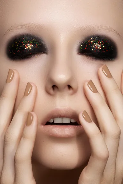 Beauty close-up portrait of sexy model woman with dark smoky eye make-up, bright glitter on eyelids, perfect beige nails polish. Cosmetics, makeup and manicure