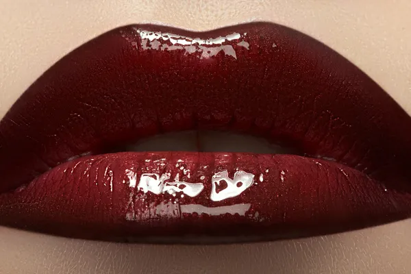 Close-up of woman\'s lips with bright fashion dark red glossy makeup. Macro lipgloss cherry make-up