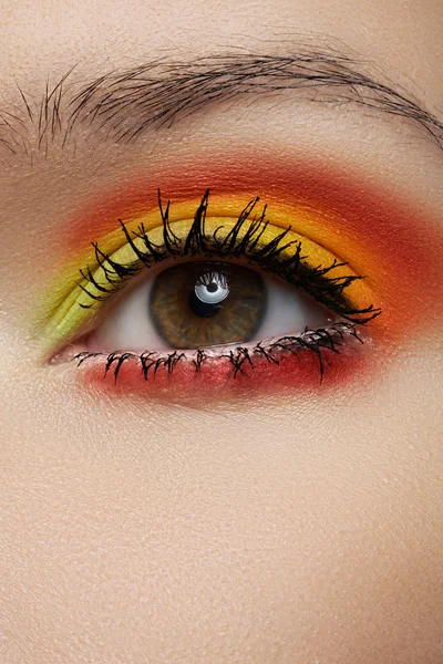 Cosmetics and beauty care. Macro close-up of beautiful green female eye with bright fashion runway make-up. Rainbow eye shadows and black eyeliner