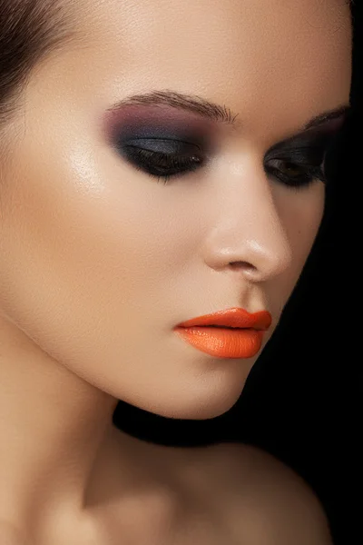 Close-up beauty portrait of attractive model face with bright make-up. Dark smoky eyes make-up and orange lips
