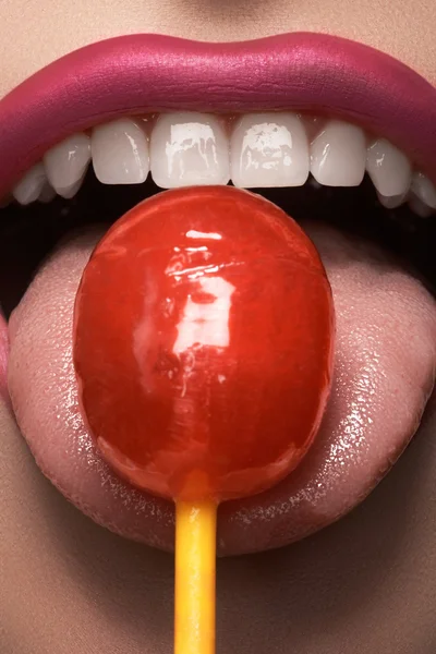 Glamour macro shoot with sexy woman\'s lips with a sweet bonbon. Beautiful bright fashion make-up. Girl licking a strawberry lollipop. Healthy teeth, funny smile