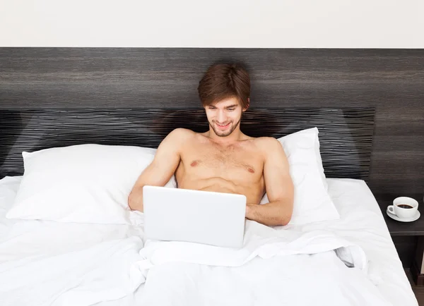 Handsome man lying on bed with laptop