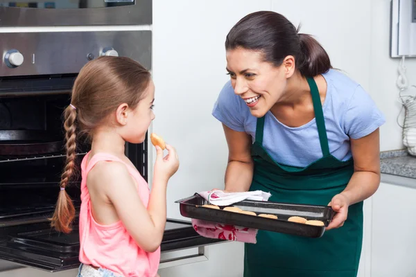 Mother and daughter taking cookies from oven