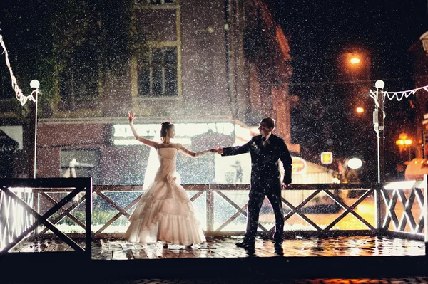 Bride and groom dancing in the night under rain