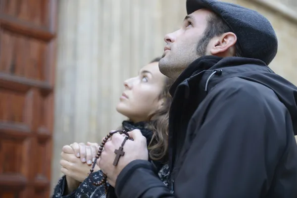 Man and woman praying in church holding prayer beads