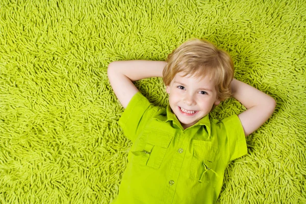 Happy child lying on the green carpet background. Boy smiling an