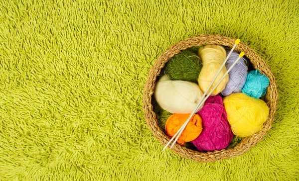 Knitting yarn balls and needles in basket over green carpet back