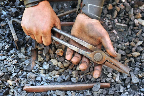 Detail of dirty hands holding pliers - blacksmith