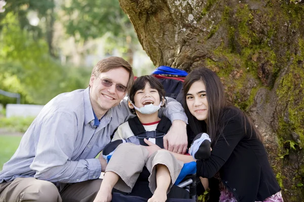 Disabled boy in wheelcahir surrounded by father and sister