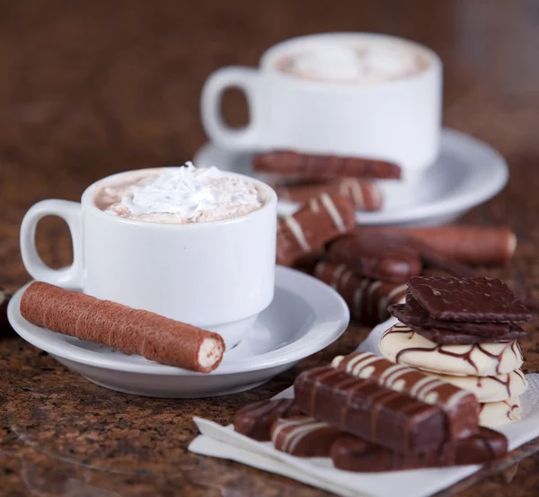Two cups of coffee or hot cocoa with chocolates and cookies on