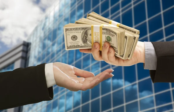 Male Handing Stack of Cash to Woman with Corporate Building