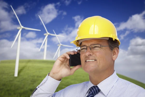 Hard Hat Wearing Engineer on Phone with Turbines Behind