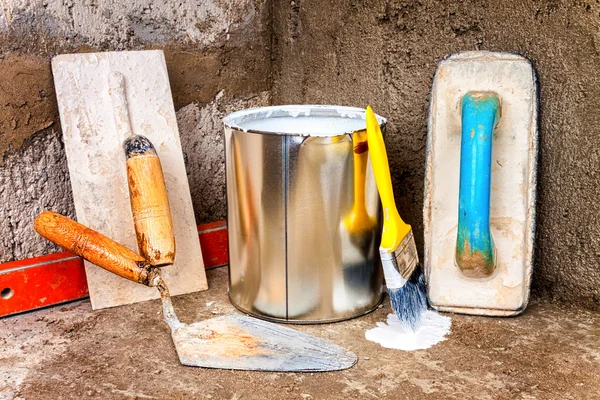 Paint can and masonry tools on a rough concrete surface