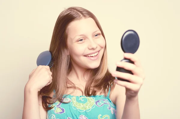 Teen girl holding hairbrush and looking at the mirror