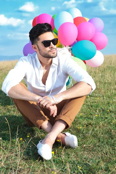 Seated casual man with balloons looks away
