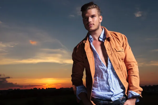 Casual man looks up with hands in pockets at sunset