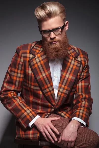 Dramatic fashion model with long beard and glasses sitting