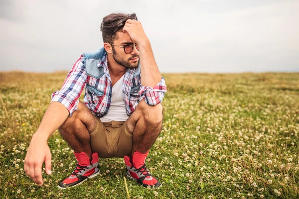 Crouched casual man in a grass field thinking