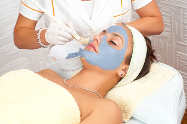 Beautiful young woman lying on massage table while facial mask is put on her face