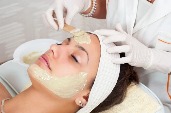Beautiful young woman lying on massage table while natural facial mask is applied on her face