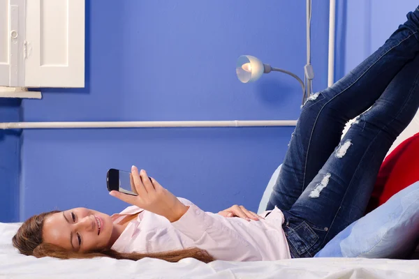 Smiling girl using mobile phone in bed