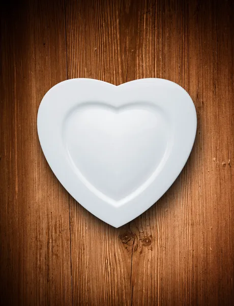 Heart form white plate on wood background