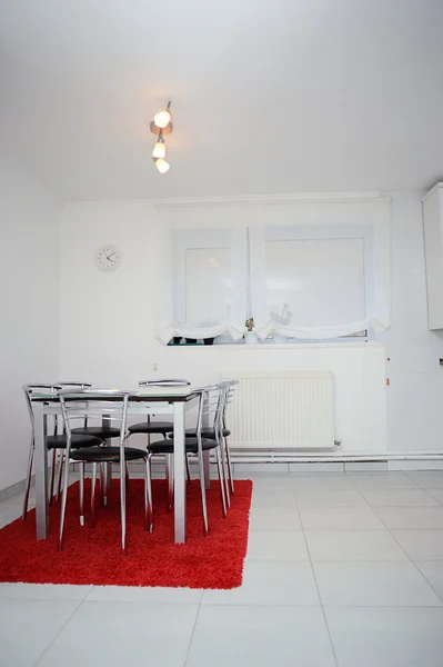 Interior of white kitchen with a table on red rug