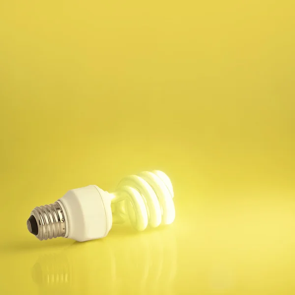 A vibrant presentation of a modern green energy-saving light bulb lit on a golden background. Plenty of copy-space - perfect for slides and presentations