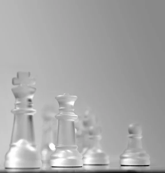 Shallow depth of field view of a chess board centered around the white queen, other pieces in soft focus in smooth grey background. Plenty of copy-space for presentation and slides