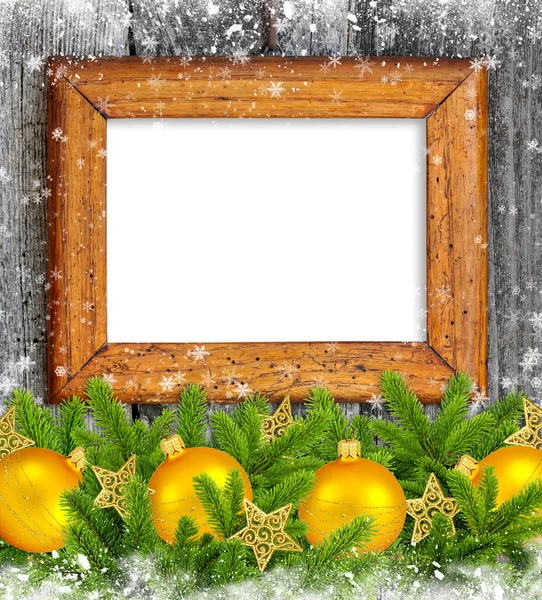 Old frame with gold christmas decoration baubles and pine on a snowbound wooden background