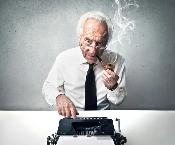Old man typing while smoking a pipe