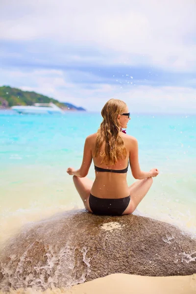 Girl in swimsuit sitting on stone backward near sea