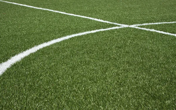 Part of a soccer field with green synthetic grass and white lines