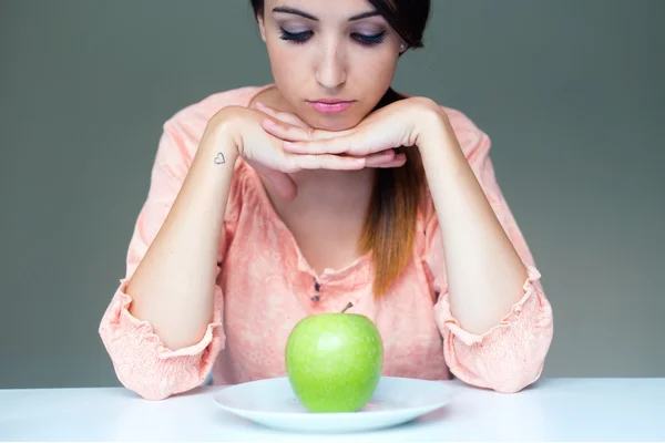 Upset brunette woman with green apple on a plate