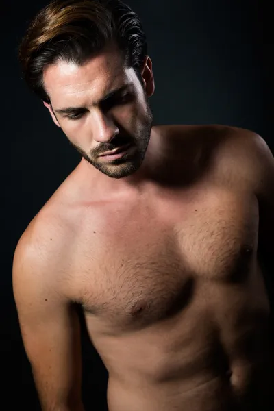 Handsome muscular male model posing over black background.