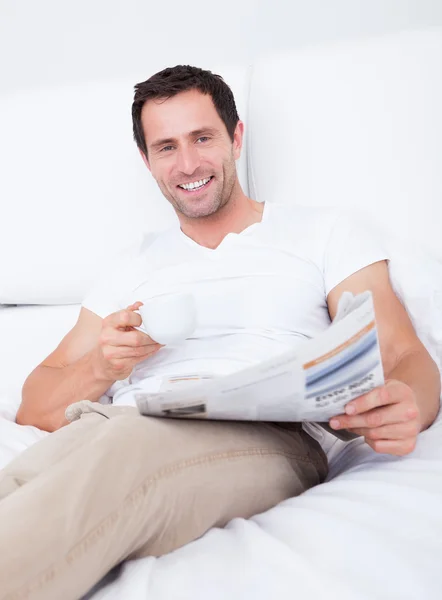 Young Man Holding Cup In Hand Reading Newspaper