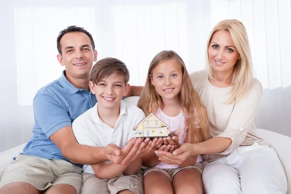 Family Sitting Holding Miniature Model Of House