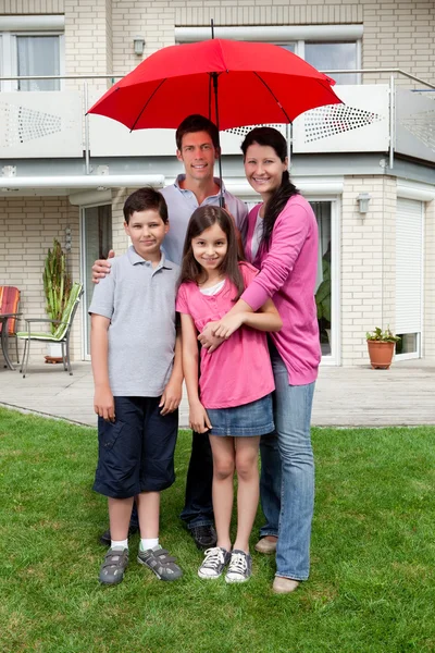 Happy family under one umbrella outside their home