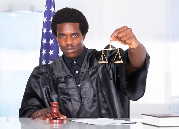 Male Judge Holding Gavel And Scale In Courtroom