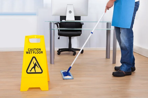 Warning notice as a janitor mops the floor