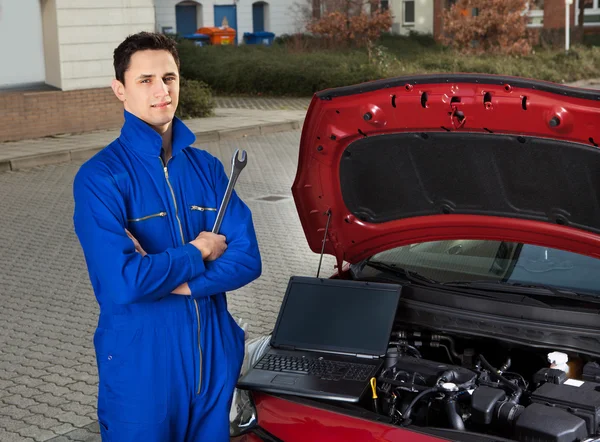 Mechanic With Arms Crossed Holding Wrench By Car