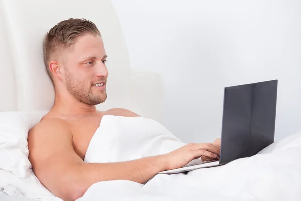 Man sitting up in bed against the pillows