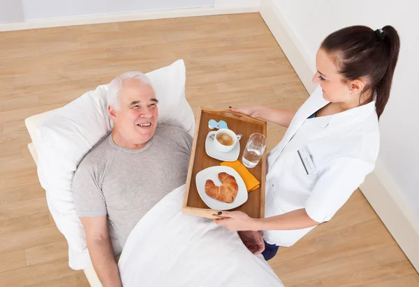 Doctor Serving Breakfast To Senior Man