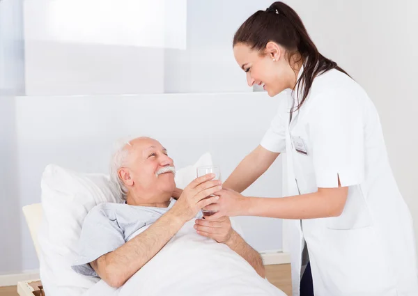 Doctor Giving Glass Of Water To Senior Man