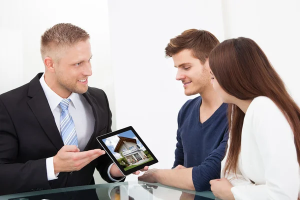 Businessman Showing House Picture To Couple On Tablet